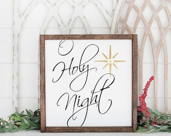May include: A white wooden sign with a brown frame, featuring the text "O Holy Night" in black cursive script with a gold star above the word "Holy". The sign is displayed on a white shelf with greenery and red berries.