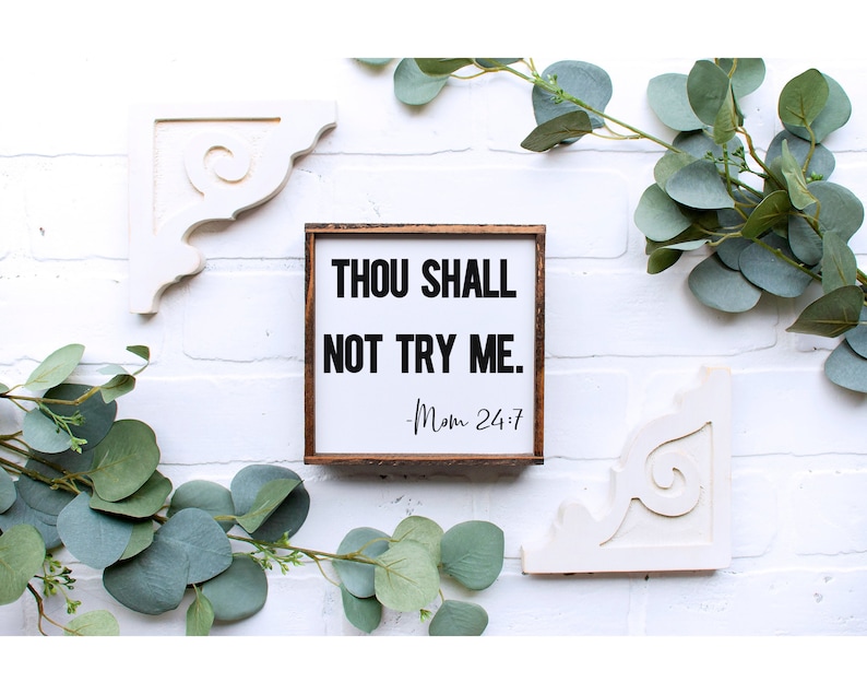 K&ouml;nnte beinhalten: Ein wei&szlig;es Holzschild mit braunem Rahmen, auf dem der Text "Thou Shall Not Try Me. -Mom 24:7" in schwarzen Buchstaben steht.
