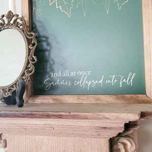 May include: A framed green canvas with a white inscription that reads "and all at once summer collapsed into fall". The canvas is decorated with gold leaf leaves.