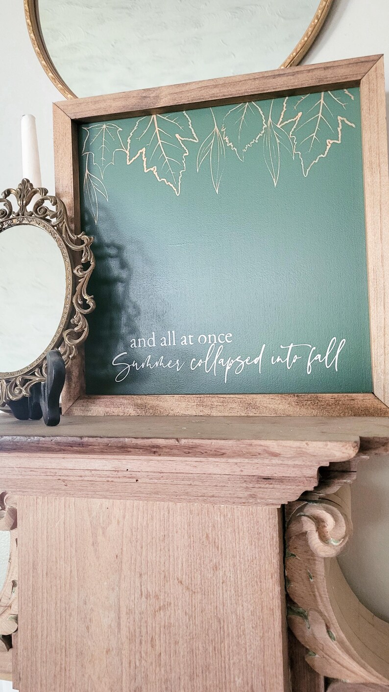 May include: A framed green canvas with a white inscription that reads "and all at once summer collapsed into fall". The canvas is decorated with gold leaf leaves.