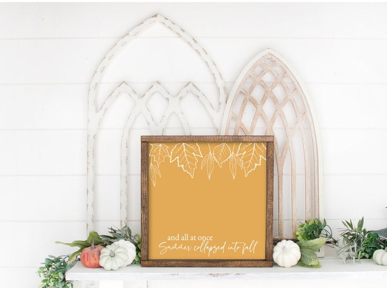 May include: A framed sign with a mustard yellow background and white outline of leaves. The text on the sign reads "and all at once summer collapsed into fall".