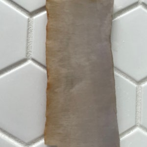 Puede incluir: Una pieza delgada y rectangular de nácar iridiscente con una textura ligeramente rugosa y un color blanco apagado.