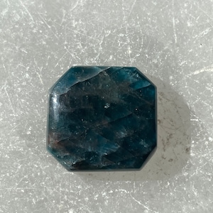 May include: A dark blue, faceted, octagonal crystal with a slightly iridescent sheen.