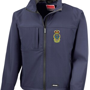 May include: Navy blue softshell jacket with a full zip, stand-up collar, and a small chest pocket. It features an embroidered emblem on the chest. The jacket has a black zip and trim.