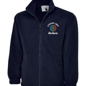 May include: Navy blue fleece jacket with a full zip and a high collar. The jacket displays the text "Stroke Unit Barbara" with a brain graphic in teal and orange. Includes two front pockets.