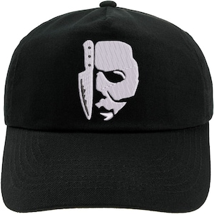 May include: Black baseball cap with a white embroidered design of a mask and a knife. The cap has a curved peak and a button on top. The design is a stylized representation of a horror movie character.