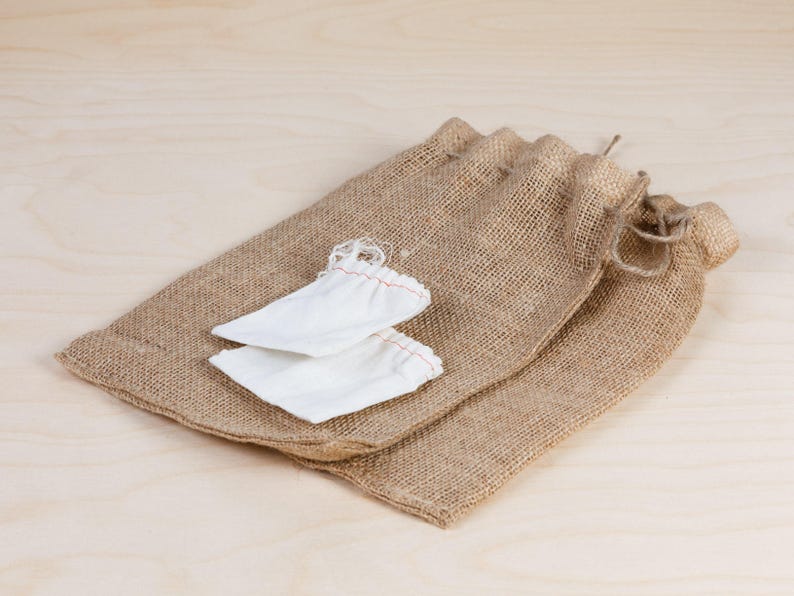 Puede incluir: Dos peque&ntilde;as bolsas de tela blanca est&aacute;n anidadas dentro de un gran saco de arpillera. El saco est&aacute; hecho de arpillera marr&oacute;n natural y tiene un cierre de cord&oacute;n.