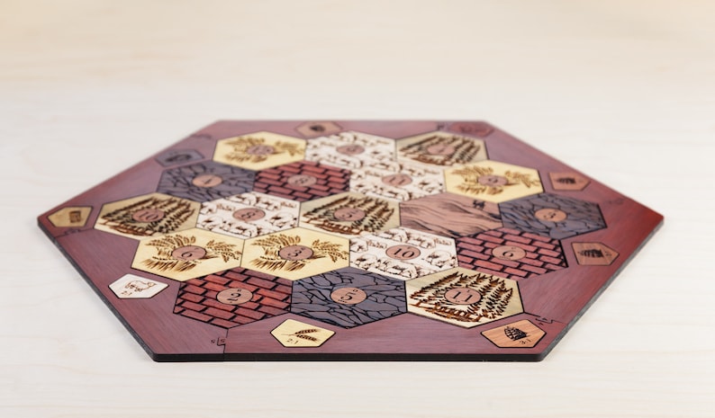 Puede incluir: Un tablero de juego hexagonal de madera con un borde rojo-marr&oacute;n. El tablero est&aacute; dividido en fichas hexagonales con diferentes dise&ntilde;os, incluyendo campos de trigo, ladrillo, madera, ovejas y piedra. Cada ficha tiene un n&uacute;mero impreso.