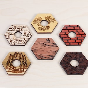 Puede incluir: Seis posavasos hexagonales de madera con diferentes dise&ntilde;os. Los posavasos est&aacute;n hechos de madera clara y tienen un agujero en el centro. Los dise&ntilde;os incluyen un campo de trigo, una manada de vacas, una escena del desierto con un camello, una pared de ladrillos, un bosque y un patr&oacute;n de tierra agrietada.