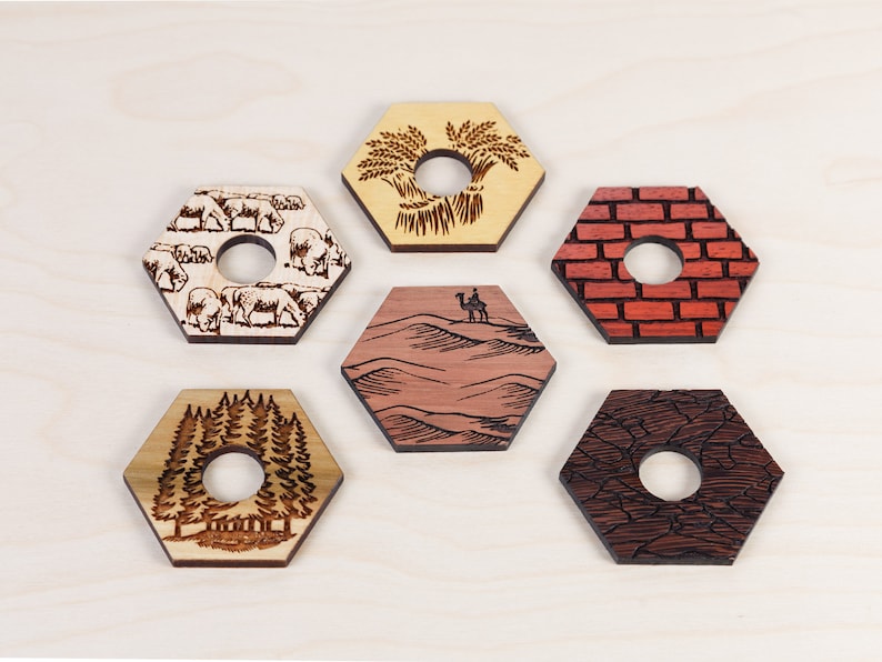 Puede incluir: Seis posavasos hexagonales de madera con diferentes dise&ntilde;os. Los posavasos est&aacute;n hechos de madera clara y tienen un agujero en el centro. Los dise&ntilde;os incluyen un campo de trigo, una manada de vacas, una escena del desierto con un camello, una pared de ladrillos, un bosque y un patr&oacute;n de tierra agrietada.