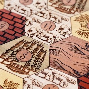 Puede incluir: Primer plano de un tablero de juego de madera con fichas hexagonales que presentan diversas ilustraciones y n&uacute;meros. Las fichas representan una pared de ladrillos, un bosque, un desierto, un campo de trigo y una manada de ovejas. Cada ficha tiene un n&uacute;mero impreso en ella, que va del 5 al 11.