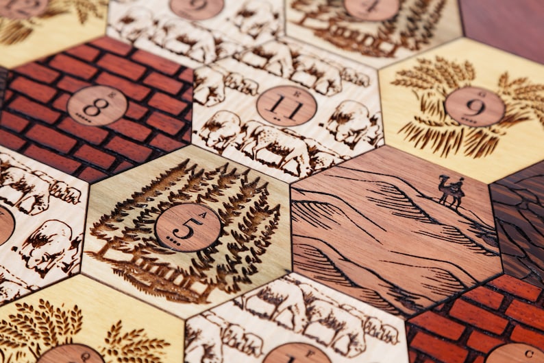 Puede incluir: Primer plano de un tablero de juego de madera con fichas hexagonales que presentan diversas ilustraciones y n&uacute;meros. Las fichas representan una pared de ladrillos, un bosque, un desierto, un campo de trigo y una manada de ovejas. Cada ficha tiene un n&uacute;mero impreso en ella, que va del 5 al 11.