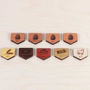 Puede incluir: Ocho fichas de juego de madera con diferentes im&aacute;genes y el texto "2:1" o "3:1" impreso en ellas. Las im&aacute;genes incluyen trigo, un tronco, una oveja y una pila de ladrillos.