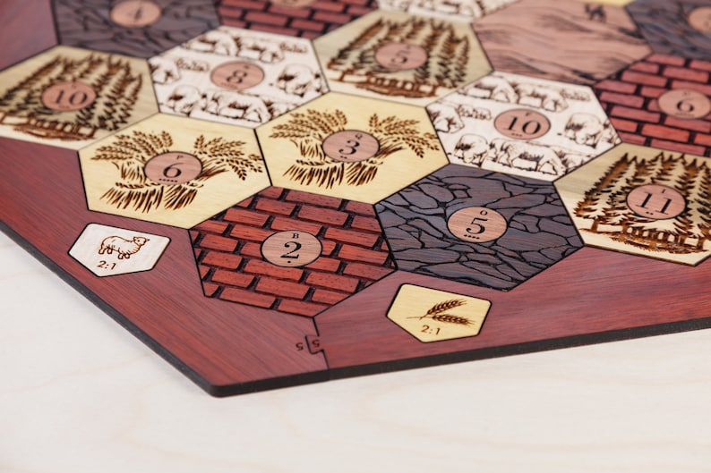 Puede incluir: Un tablero de juego de madera con fichas hexagonales que representan diferentes recursos, incluyendo trigo, ovejas, madera y piedra. Cada ficha tiene un n&uacute;mero impreso, que va del 2 al 11. El tablero est&aacute; hecho de madera roja oscura y tiene un borde negro.