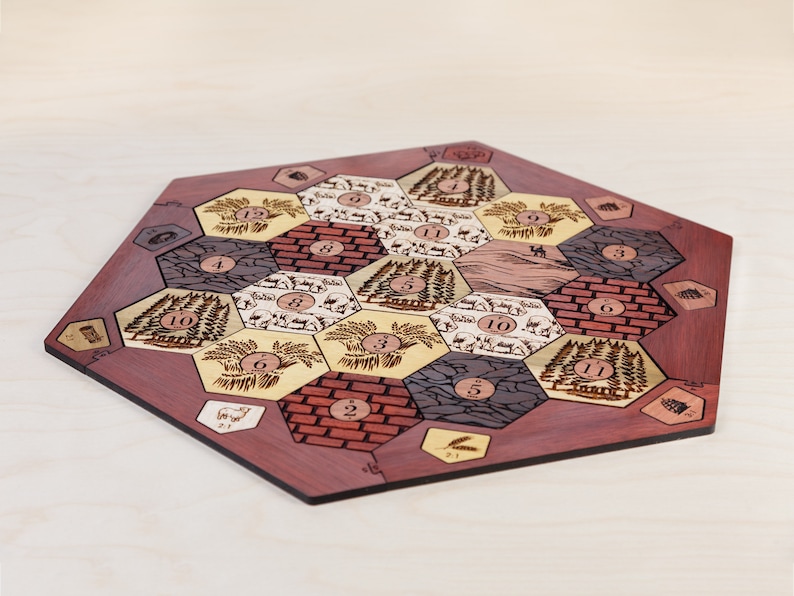 Puede incluir: Un tablero de juego hexagonal de madera con un borde de caoba roja. El tablero est&aacute; dividido en 19 fichas hexagonales, cada una con un tipo de recurso diferente: trigo, ovejas, madera, ladrillo y mineral. Cada ficha tiene un n&uacute;mero del 2 al 12.