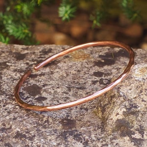 Peut inclure: Un bracelet simple en cuivre martelé. Le bracelet est posé sur une roche grise et rugueuse.