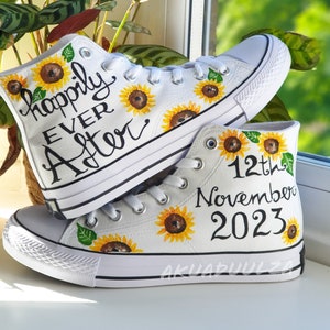 May include: A pair of white high-top canvas shoes with sunflower designs and hand-painted text. One shoe says "Happily Ever After" and the other says "12th November 2023".