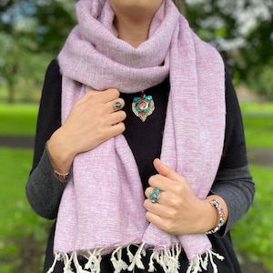 May include: A soft, pink scarf with white fringe. The scarf is made of a lightweight material and is perfect for layering.