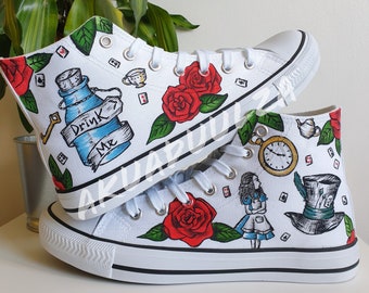 May include: White high-top canvas shoes with hand-painted Alice in Wonderland themed designs. The shoes feature red roses, a pocket watch, a teacup, a bottle with the words "Drink Me", Alice, and the Mad Hatter's hat.