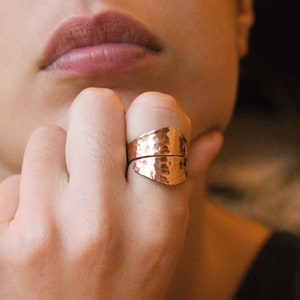 May include: A hammered copper ring with a unique design. The ring is worn on the index finger of a person's hand.
