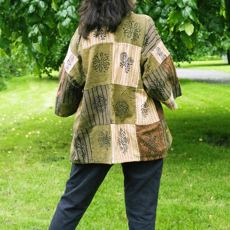 Peut inclure: Veste patchwork aux tons verts, marron et beige. La veste pr&eacute;sente une vari&eacute;t&eacute; de carr&eacute;s &agrave; motifs avec des motifs floraux et abstraits. Les manches sont aux trois quarts. La personne porte un pantalon bleu fonc&eacute;.
