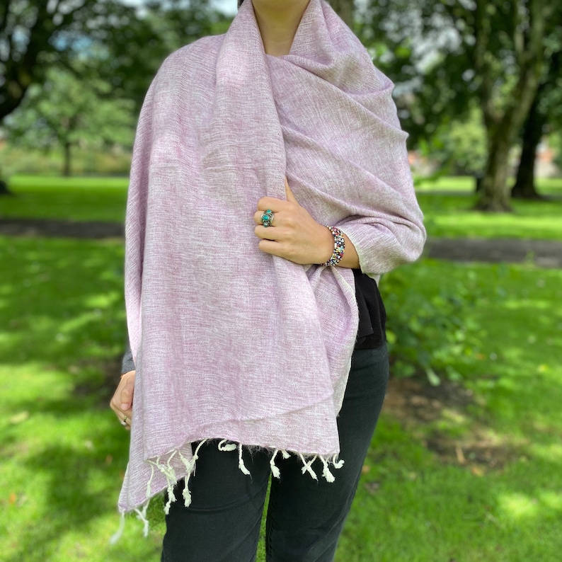 May include: A soft, light purple shawl with white fringe. The shawl is made of a lightweight fabric and is perfect for layering.