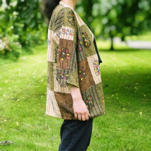 Peut inclure: Veste patchwork aux tons verts et bruns, orn&eacute;e de motifs floraux et g&eacute;om&eacute;triques. La veste a des manches trois-quarts et une coupe ample. Le design int&egrave;gre diverses textures et couleurs de tissu, cr&eacute;ant une esth&eacute;tique boh&egrave;me. La veste est port&eacute;e sur un haut noir.