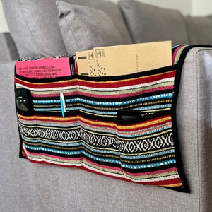 Könnte beinhalten: Ein mehrfarbiger, gestreifter Couch-Armlehnen-Organizer mit Taschen für Fernbedienungen, Telefone und andere Gegenstände. Der Organizer ist aus Stoff und hat einen schwarzen Besatz. Der Text auf dem rosa Zettel lautet "FARE LA SPESA ORGANIZZARE IL PRANZO O LA CENA EPOL NATURALMENTE, CUCINARE A VOLTE PUÒ NON ESSERE SOPRATTUTTA SE DOBBIAMO PENSARE ANCHE".