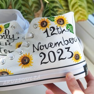 May include: White canvas high-top sneakers with a hand-painted design featuring sunflowers and the text "12th November 2023".
