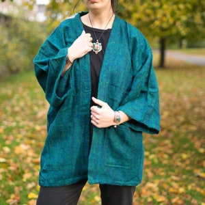 Puede incluir: Una chaqueta de estilo kimono azul turquesa con un patrón verde oscuro. La chaqueta tiene manga larga y un corte holgado.