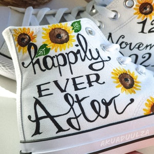 May include: White canvas high-top sneakers with black hand-painted lettering that reads "happily ever after". The sneakers are decorated with yellow sunflowers and the date "12 November 2022".
