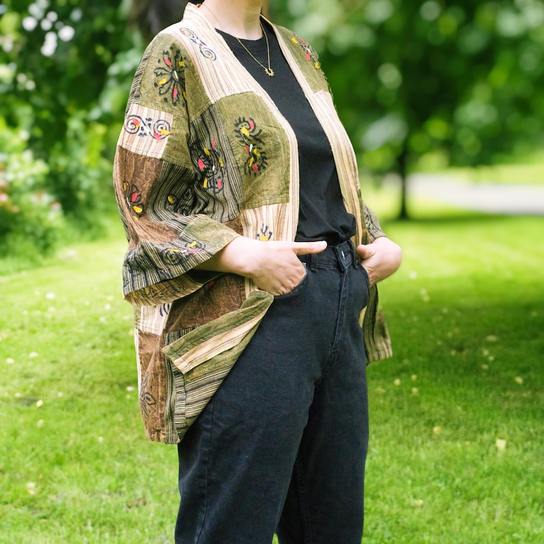 Peut inclure: Veste kimono patchwork aux tons verts, marron et beige. La veste pr&eacute;sente des motifs floraux brod&eacute;s et un devant ouvert. La personne porte un haut noir et un jean d&eacute;lav&eacute; fonc&eacute;. V&ecirc;tement d'ext&eacute;rieur &eacute;l&eacute;gant.
