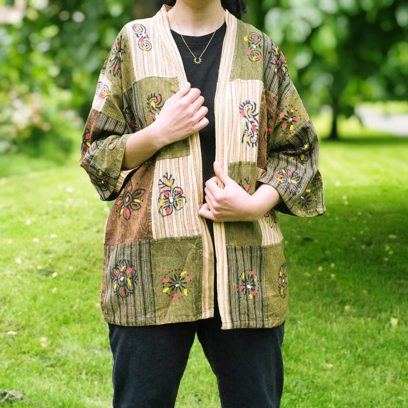 Peut inclure: Veste de style kimono en patchwork dans les tons de vert, marron et beige. La veste pr&eacute;sente des broderies florales et un design ample et ouvert. Les manches sont aux trois quarts et le v&ecirc;tement semble &ecirc;tre fait d'un tissu l&eacute;ger.