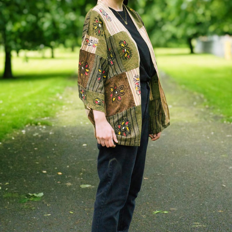 Peut inclure: Veste kimono patchwork aux tons verts et bruns. La veste pr&eacute;sente des carr&eacute;s &agrave; motifs avec des broderies florales. Les manches sont aux trois quarts et la veste est ouverte sur le devant. Le v&ecirc;tement est port&eacute; sur un haut noir et un jean fonc&eacute;.