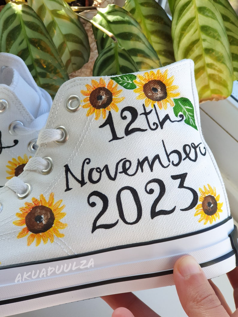 May include: White canvas high-top sneakers with hand-painted sunflowers and the text "12th November 2023".