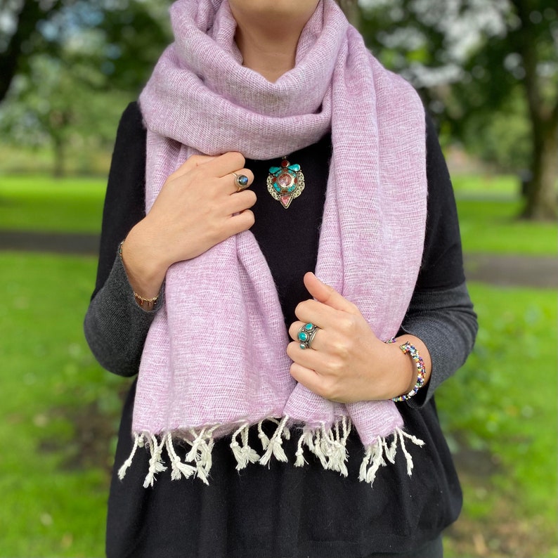 May include: A soft, pink scarf with white fringe. The scarf is made of a lightweight material and is perfect for layering.