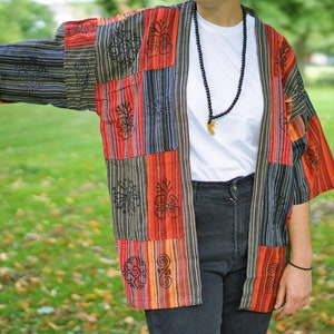 May include: A patchwork kimono-style jacket in a vibrant mix of colors including red, orange, black, and blue. The jacket features vertical stripes and floral patterns. The sleeves are short, and the overall style is casual and bohemian.