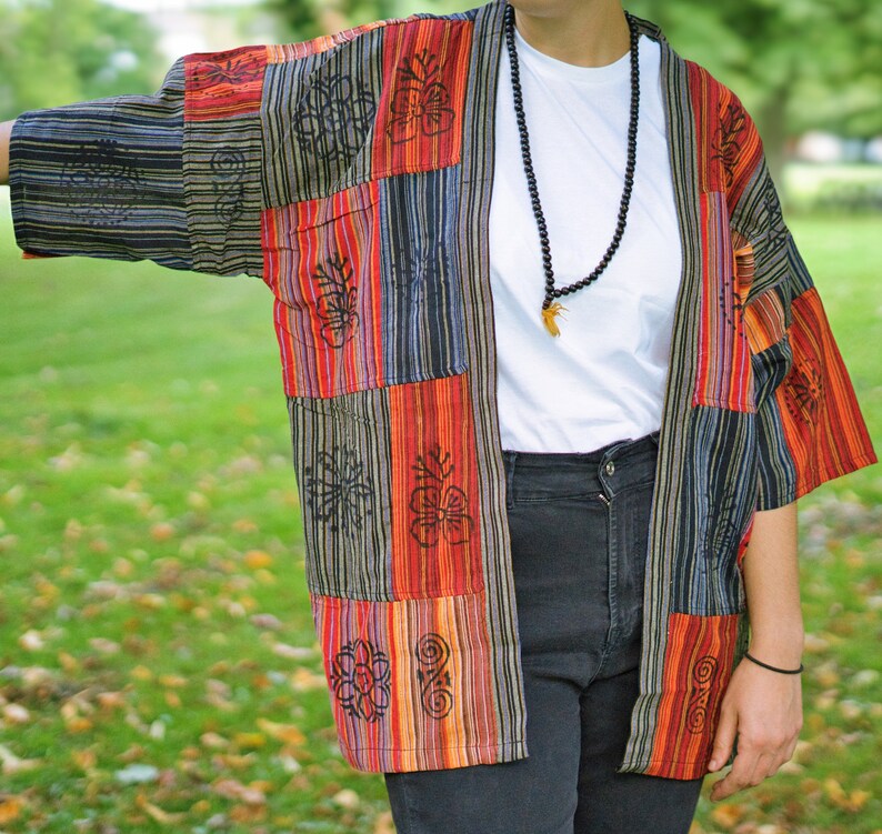 May include: A patchwork kimono-style jacket in a vibrant mix of colors including red, orange, black, and blue. The jacket features vertical stripes and floral patterns. The sleeves are short, and the overall style is casual and bohemian.
