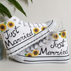May include: A pair of white high-top canvas shoes with black laces and the words "Just Married" written on them. The shoes are decorated with painted sunflowers.