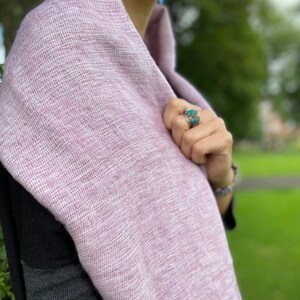 May include: A soft, light purple scarf made of a woven fabric. The scarf is draped around a person's neck and shoulders.