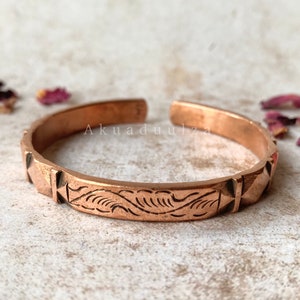 May include: A copper bracelet with a decorative etched design and a row of pyramid-shaped accents on each side.