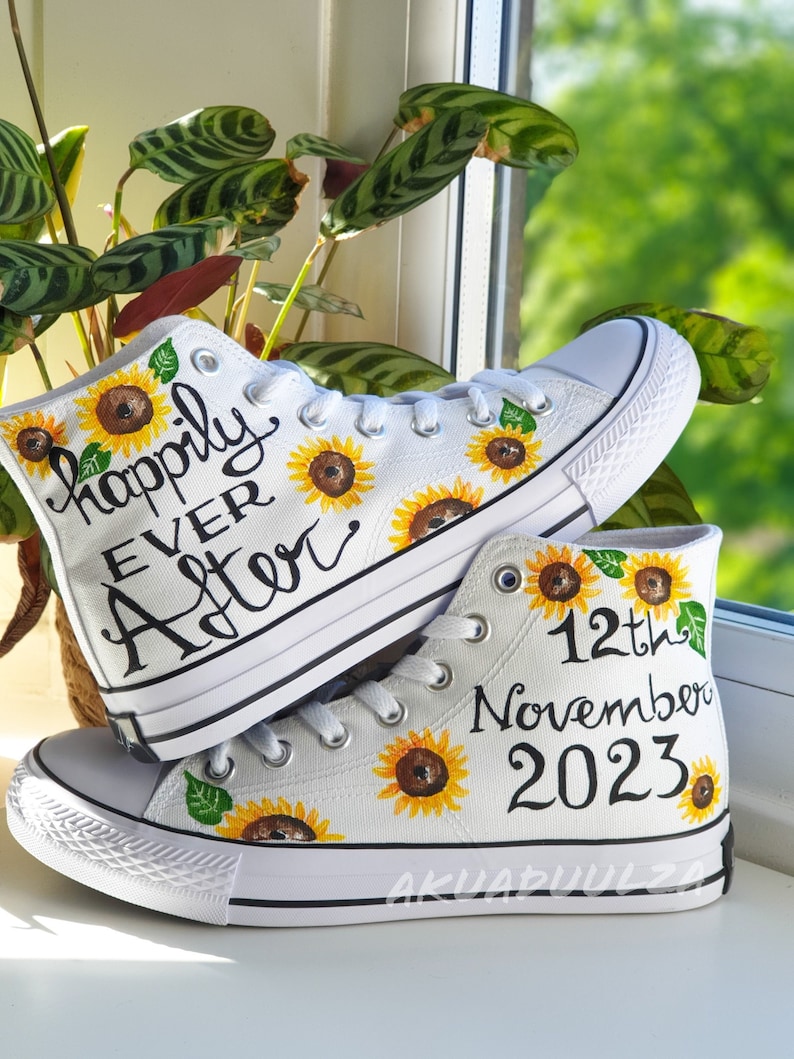 May include: A pair of white high-top canvas shoes with sunflower designs and hand-painted text. One shoe says "Happily Ever After" and the other says "12th November 2023".