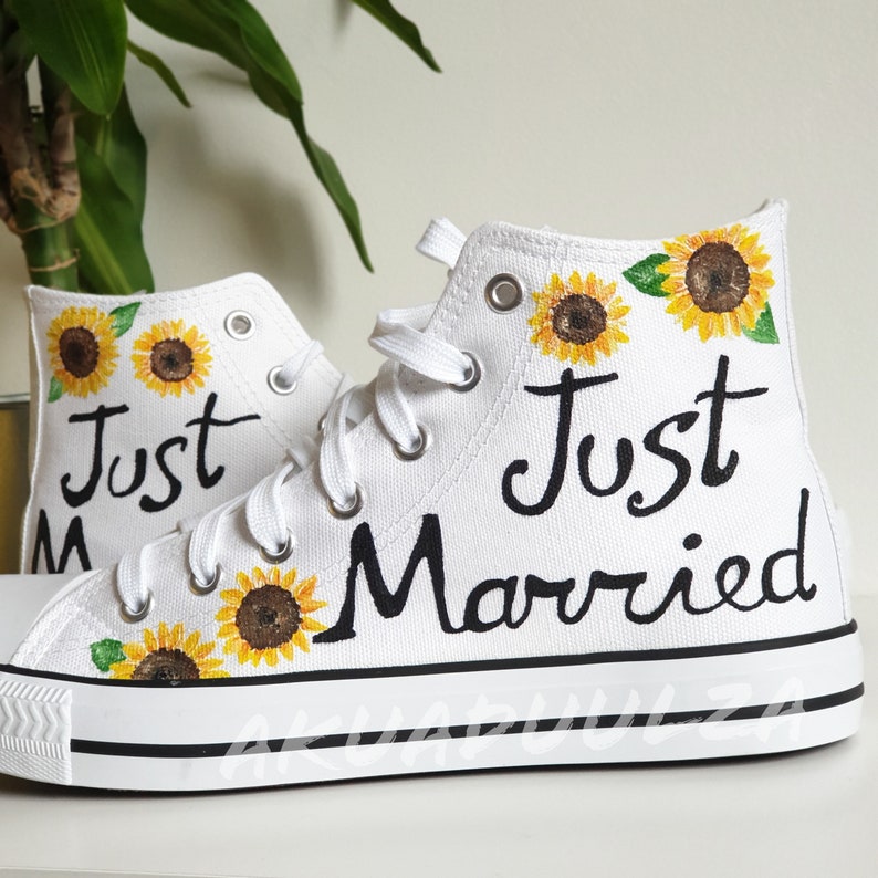 May include: White high-top canvas sneakers with the words "Just Married" painted in black. The shoes are decorated with yellow sunflowers.