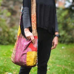 Può includere: Una borsa tote in patchwork colorata con un motivo floreale. La borsa è realizzata con tessuti diversi e ha una tracolla lunga.