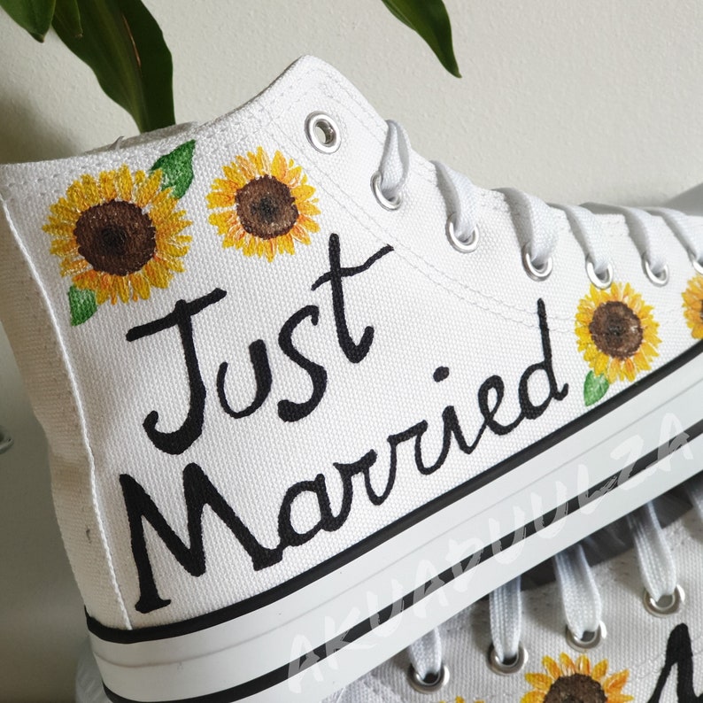 May include: White high-top canvas shoes with black painted text "Just Married" and sunflower designs.