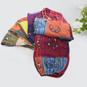 Op de afbeelding: Een stapel kleurrijke patchwork broeken met verschillende bloemen- en geometrische patronen. De broeken zijn gemaakt van een zachte, lichte stof en hebben een comfortabele elastische tailleband.