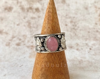 Peut inclure: Une bague en argent avec une pierre ovale rose sertie au centre. La bague est décorée de feuilles et de perles en argent.