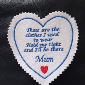 May include: White felt heart-shaped patch with blue stitching around the edges. The patch has blue embroidered text that reads "These are the clothes I used to wear Hold me tight and I'll be there Mum" with a small red embroidered heart below the text.