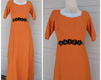 May include: A long orange dress with a velvet flower belt. The dress has a square neckline and short sleeves.