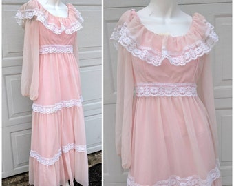 May include: A long, pink maxi dress with white lace trim. The dress has a scoop neckline, long sleeves, and a tiered skirt.